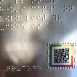 close-up from the Byderhand project: a piece of metal plate with braille text and a QR code surrounded by textured lines